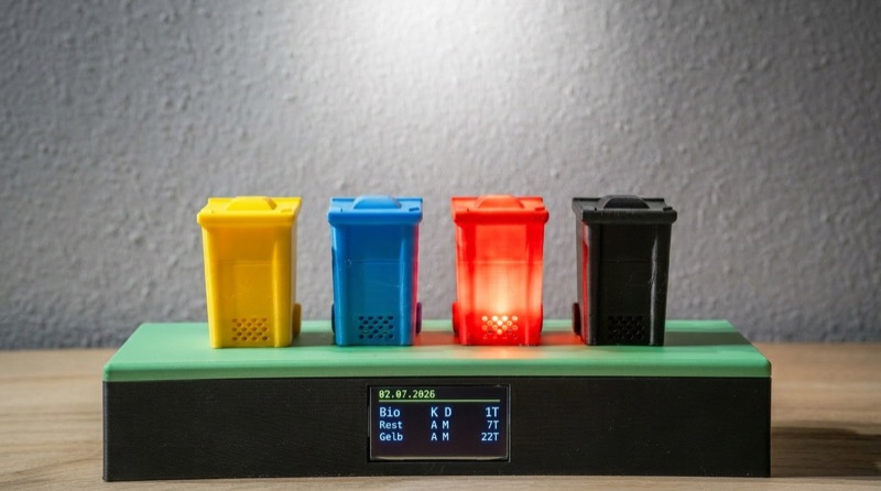 Digitaler Müllkalender: vier bunte Mini-Tonnen auf einem Gehäuse, die rote leuchtet, darunter ein Display mit den nächsten Abholterminen